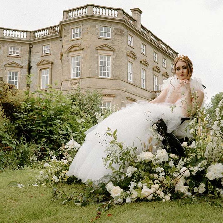 Bride in a wheelchair wearing a tulle wedding dress and gold headdress with white and green flowers decorating the wheels