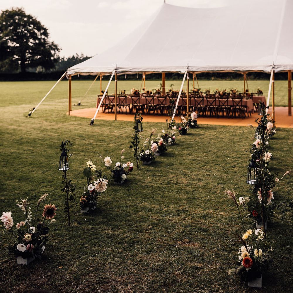 Marquee garden wedding reception in field with long wooden tables with dusky pink tablecloth, wooden chairs and florals for Cornish wedding