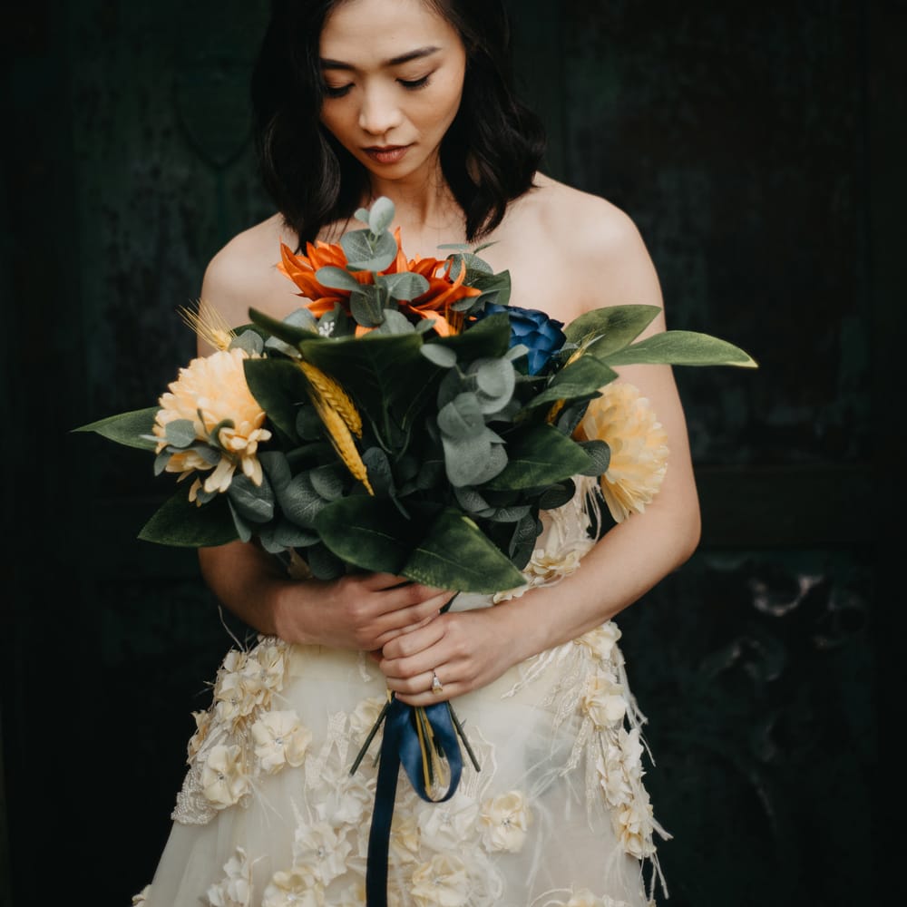 Bride in strapless feathered wedding dress and bridal headpiece holds large tropical bridal bouquet as she stands in doorway at Wellbeing Farm wedding