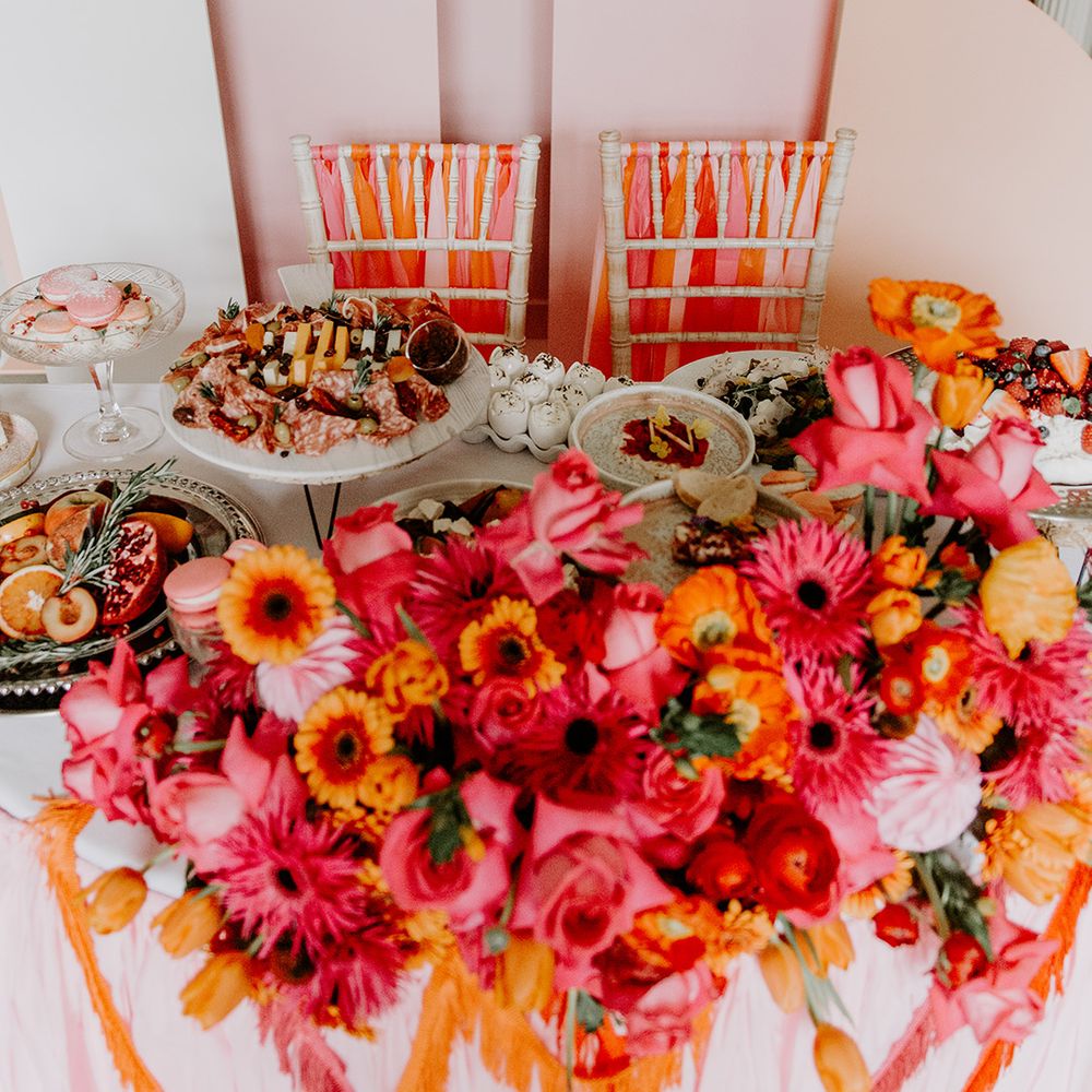 Sweetheart table with pink geometric backdrop, red, pink and orange flower arrangement and bistro food by Baba Ganoush 