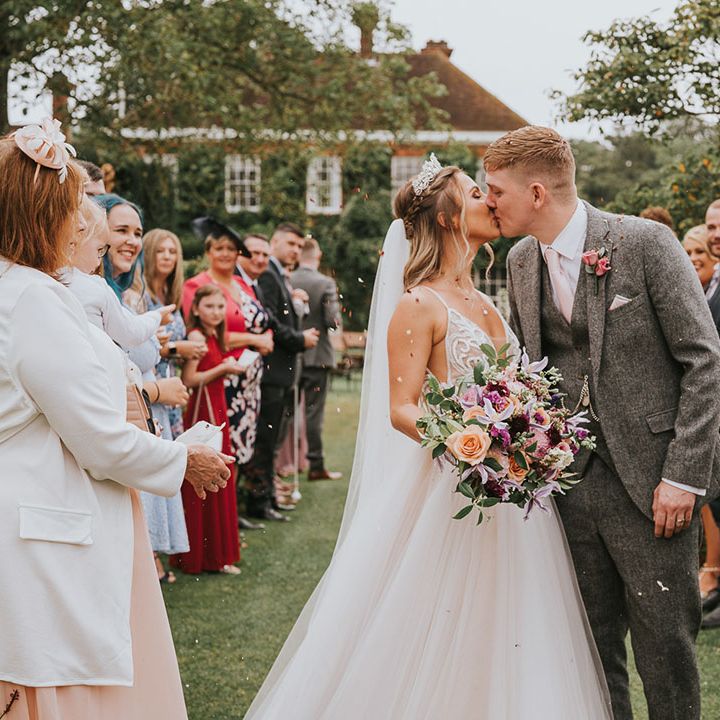 Bride and groom share a kiss in front of their wedding guests outside of wedding venue at country house