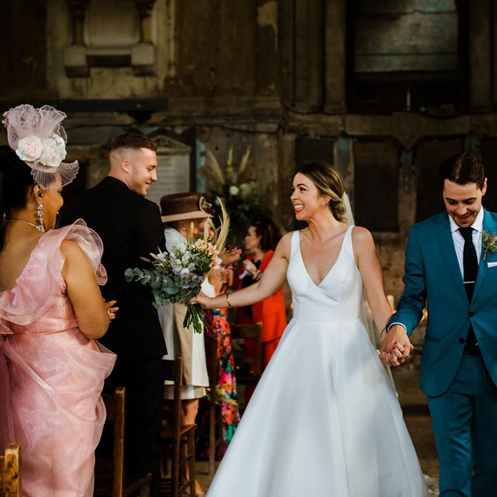 Groom in blue suit walks back down the aisle with bride in simple v neck wedding dress at chapel wedding