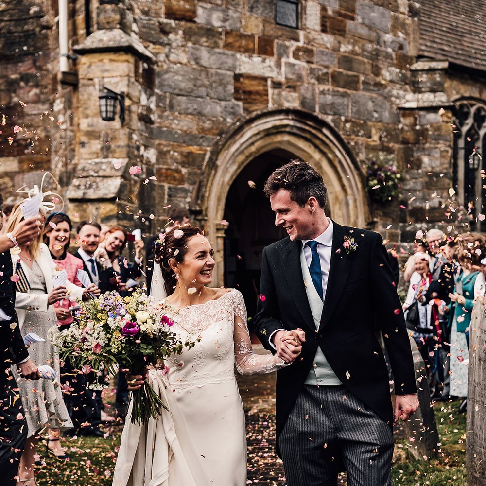 Bride and groom have confetti exit from traditional church wedding with pink rose petals 