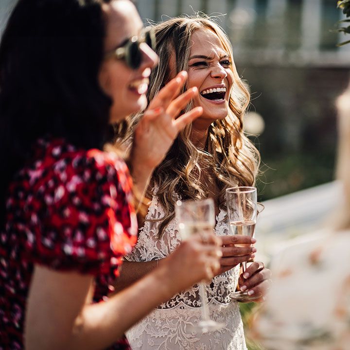 Bride laughs and socialises with wedding guests holding glass of champagne 