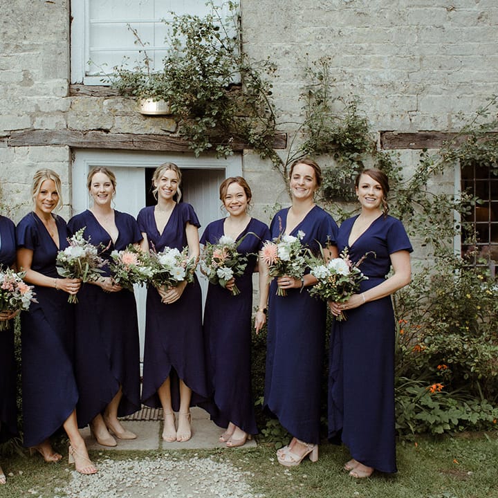 Seven bridesmaids in navy blue dresses with butterfly sleeves and nude wedding shoes holding white and pink bouquets 