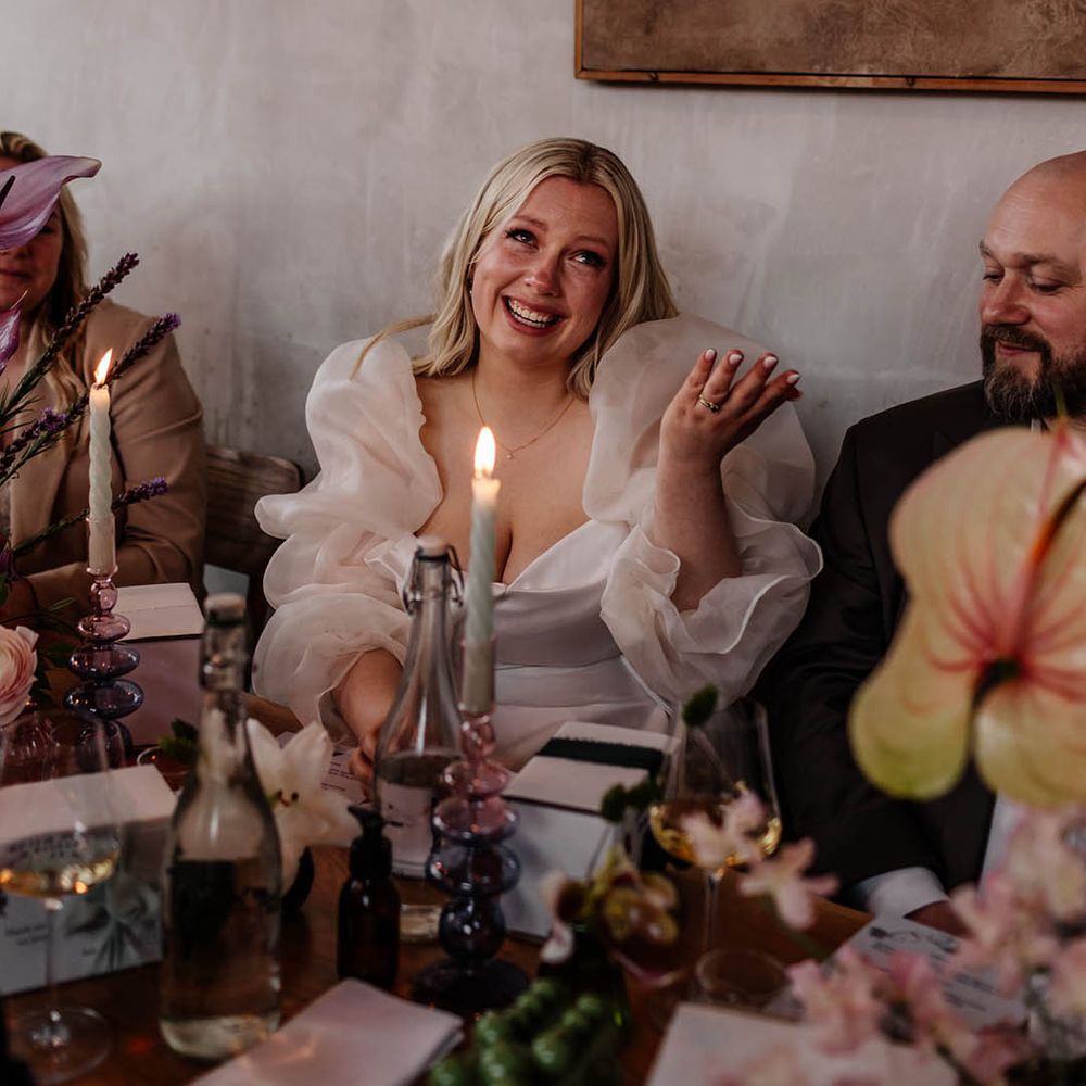 emotional bride in long sheer sleeve wedding dress at wedding reception smiling during the speeches 