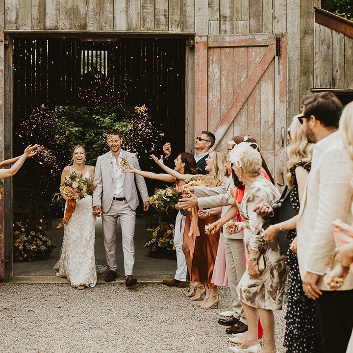 Bride and groom walk out of the Nancarrow Farm wedding venue in Cornwall as wedding guests throw confetti 