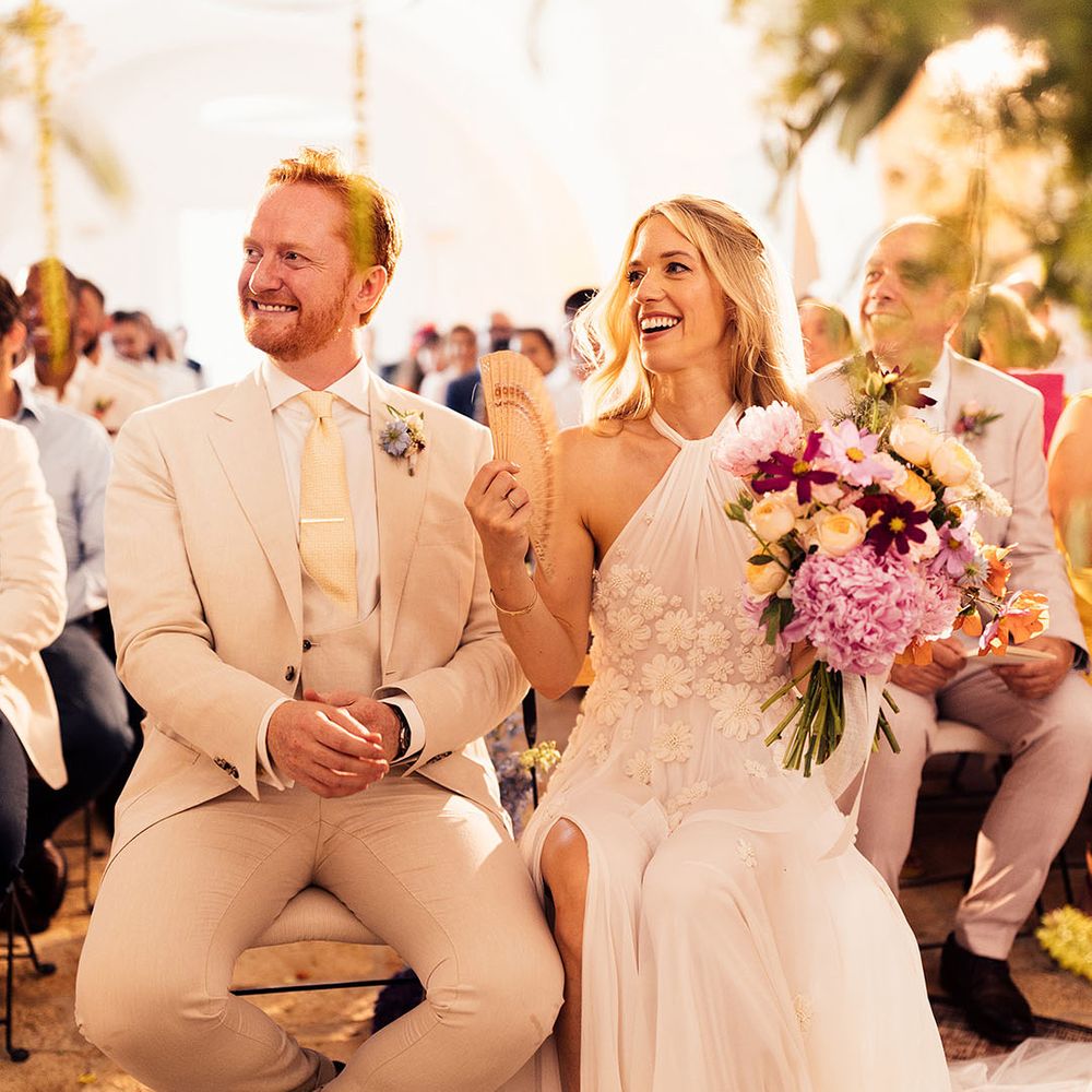 Bride and groom sit for their wedding ceremony with a fan in the hot Italian summer weather 