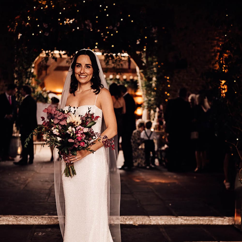 Bride in a beaded sparkle wedding dress with train holding a dark pink bouquet of flowers for barn wedding 