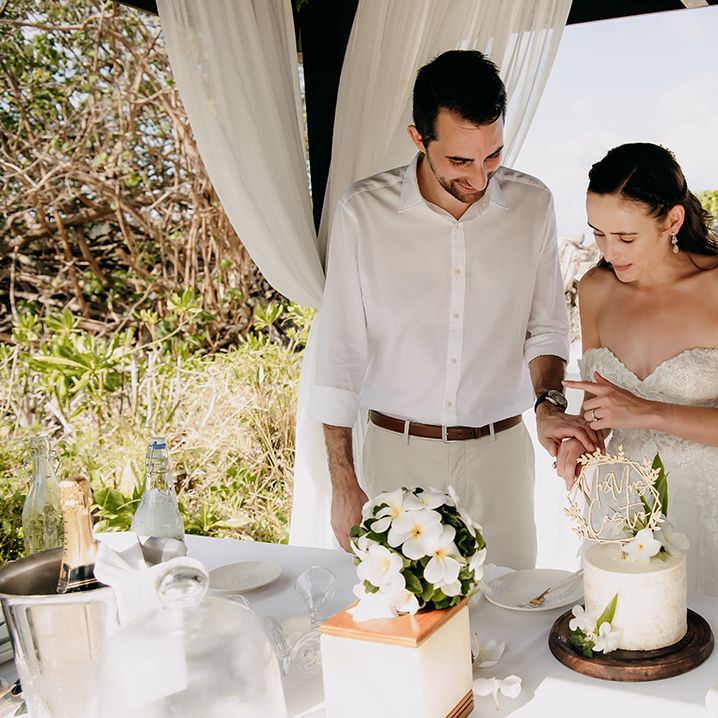 Bride and groom cutting their single tier buttercream wedding cake with personalised gold laser cut wedding topper and tropical flower decorations