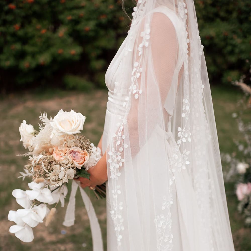Close up of the bride's wedding veil with leaf and floral design holding a neutral bouquet