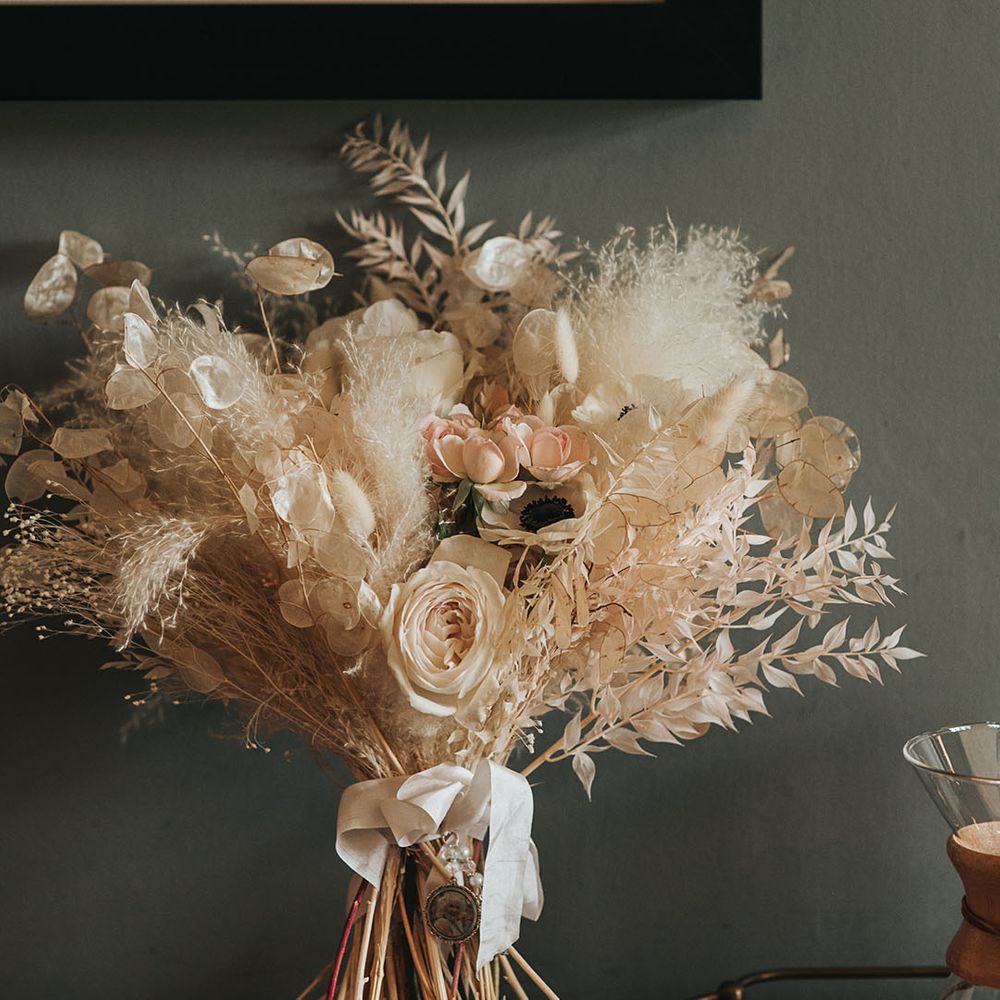 Bride's white bouquet with roses, poppies, and dried grass tied up with white ribbon 