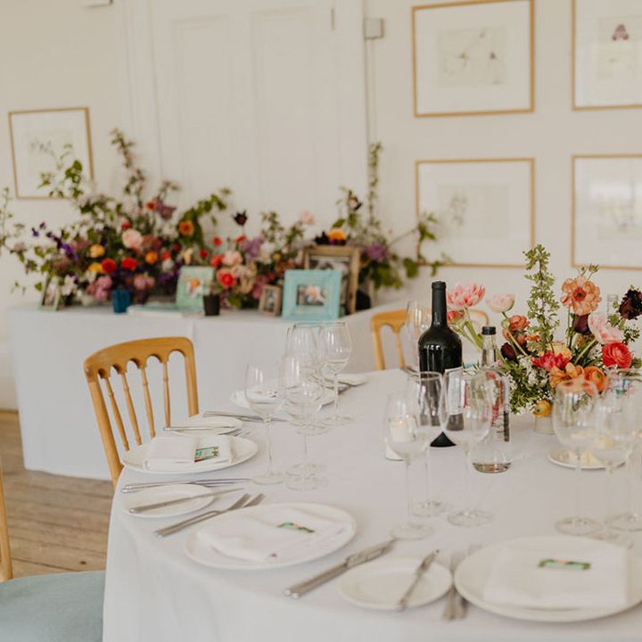 Bright floral centrepieces sit in the middle of round tables covered in white tablecloth complete with white candles 