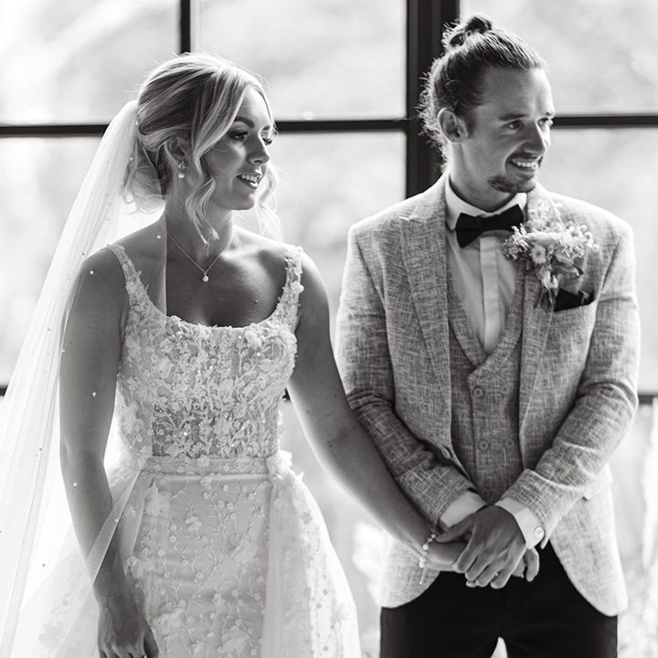 The bride in an applique embellished Eleganza Sposa Iconica wedding dress with pearl veil standing with groom in three piece suit at Hidden River Cabins