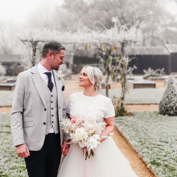 Groom in light grey suit jacket with the bride in a beaded top and skirt bridal separates with a pink and white rose bouquet 