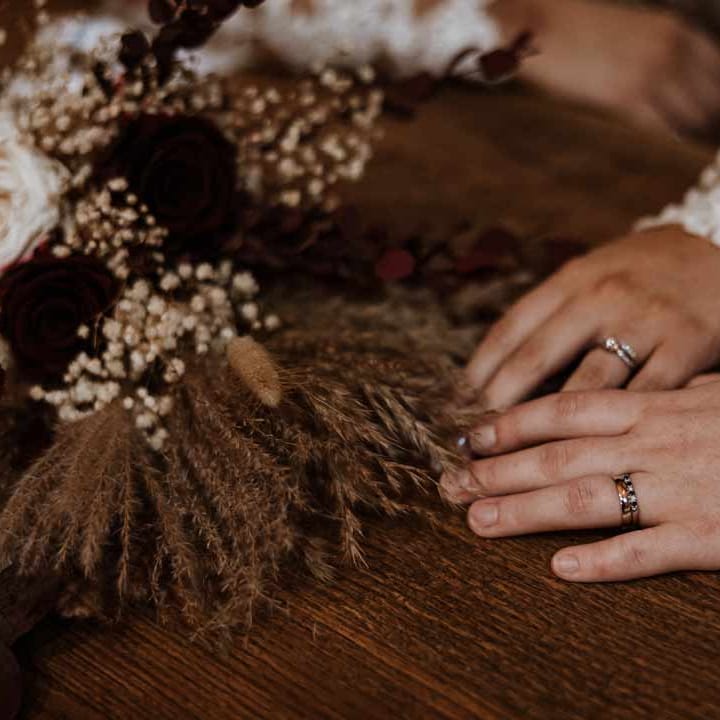 Brides showing off their wedding rings on wooden table with dried flower, pampas grass and baby's breath flower arragements 