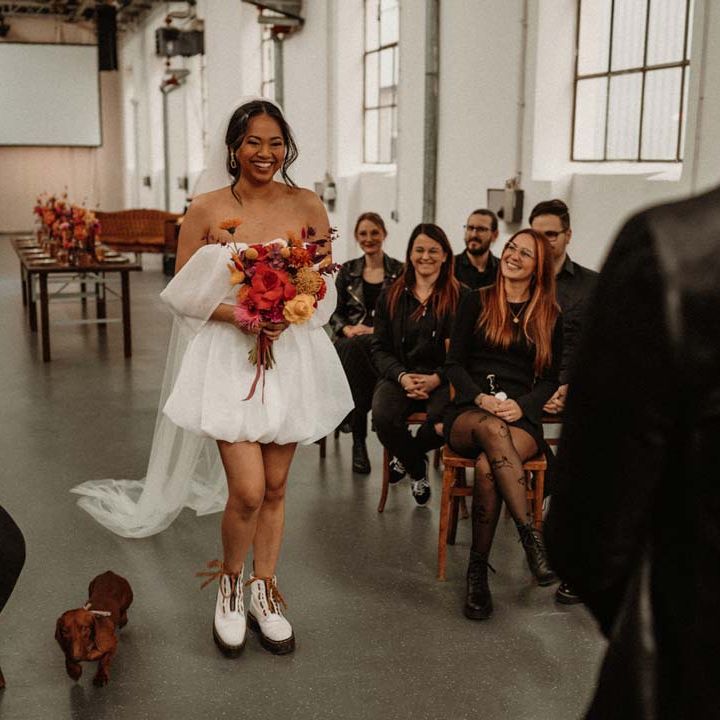 Bride in off shoulder tulle short wedding dress with church length veil and white platform Dr Martens wedding shoes holding vibrant pink and orange bridal bouquet walking down the aisle towards groom standing by vinyl wedding arch