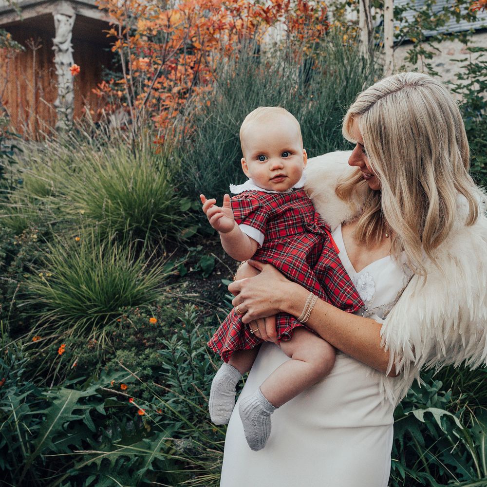 Bride holds baby wearing Tartan dress on wedding day 
