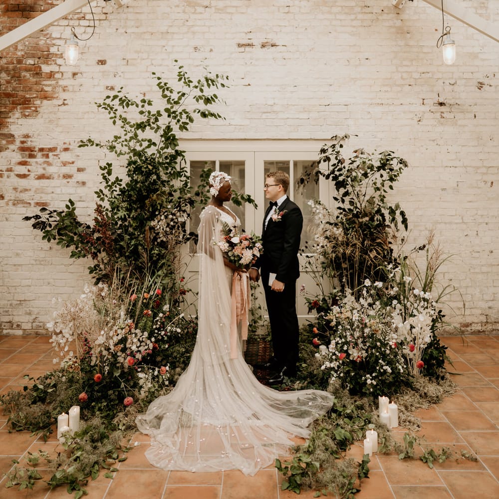 Bride and groom exchanging vows at a vertical wildflower arrangement with foliage and pillar candles altar 
