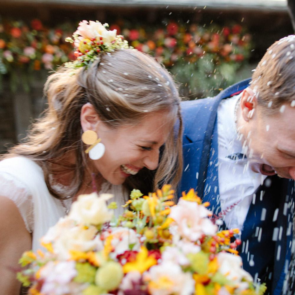 The bride and groom laughing as they have rice confetti thrown over them