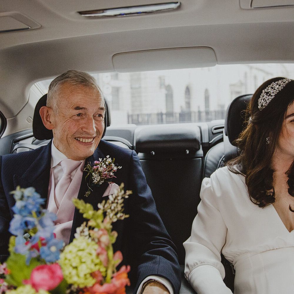 Bride wearing long sleeve wedding dress on the way to her wedding in the car with father of the bride