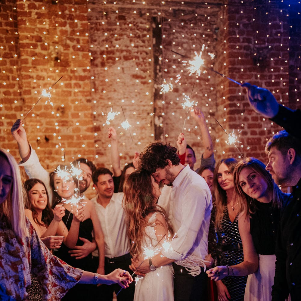 The bride and groom cuddle surrounded by their guests who are holding up sparklers