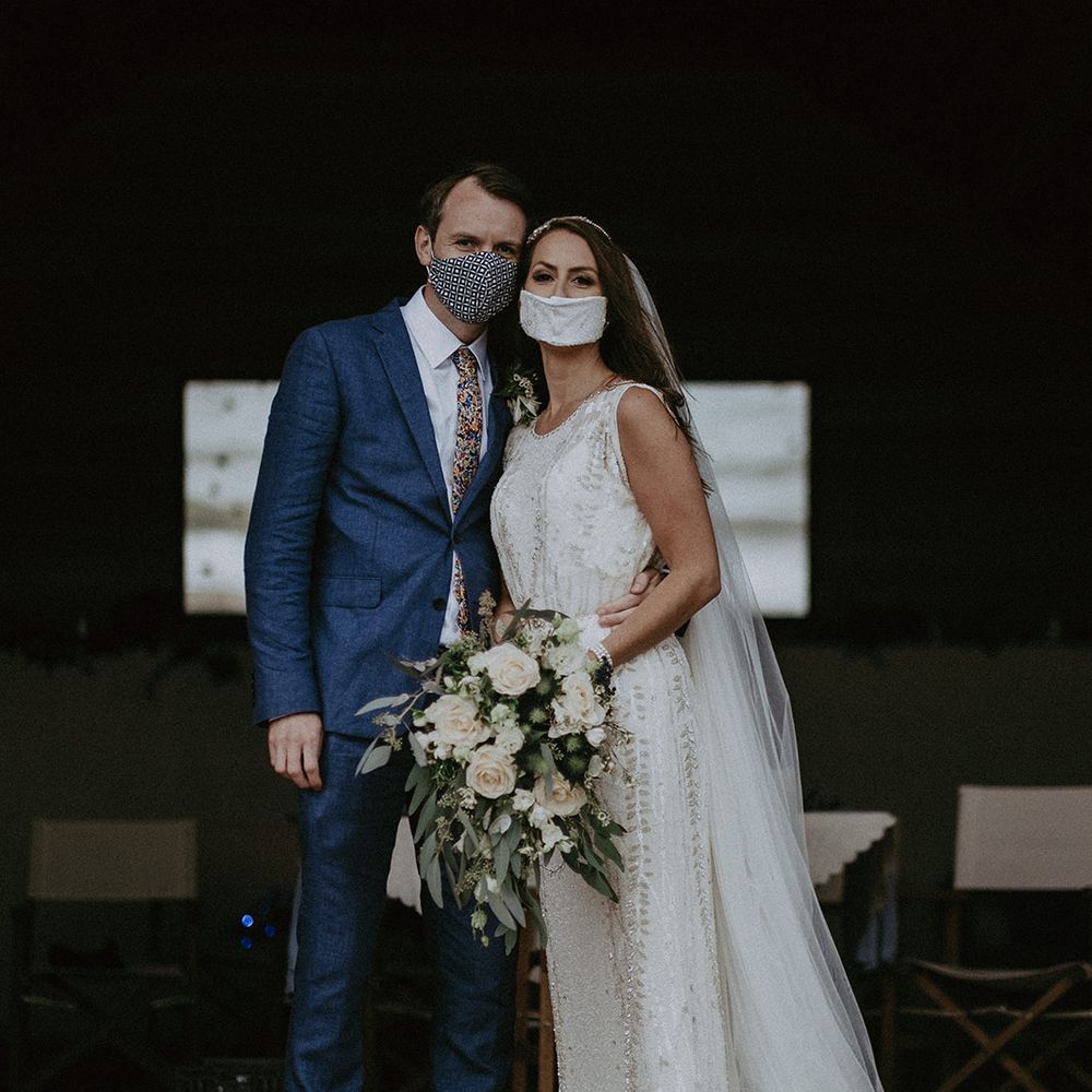 Bride & groom stand together whilst wearing face masks on the day of their wedding
