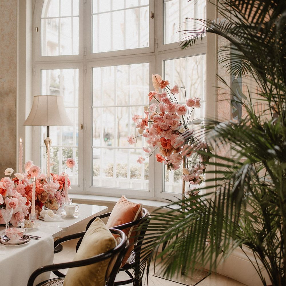 Luxurious peach wedding flowers tablescape with pink tapered candles, in between tropical palm tree plants with standing pink flower display