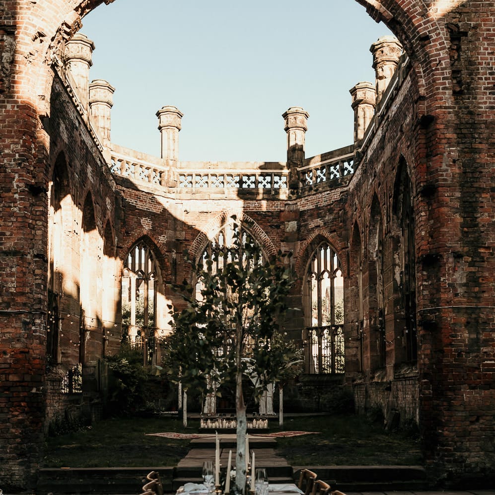 Wedding reception at St Lukes Bombed Out Church in Liverpool with greenery table runner, trees and pillar candle decor 