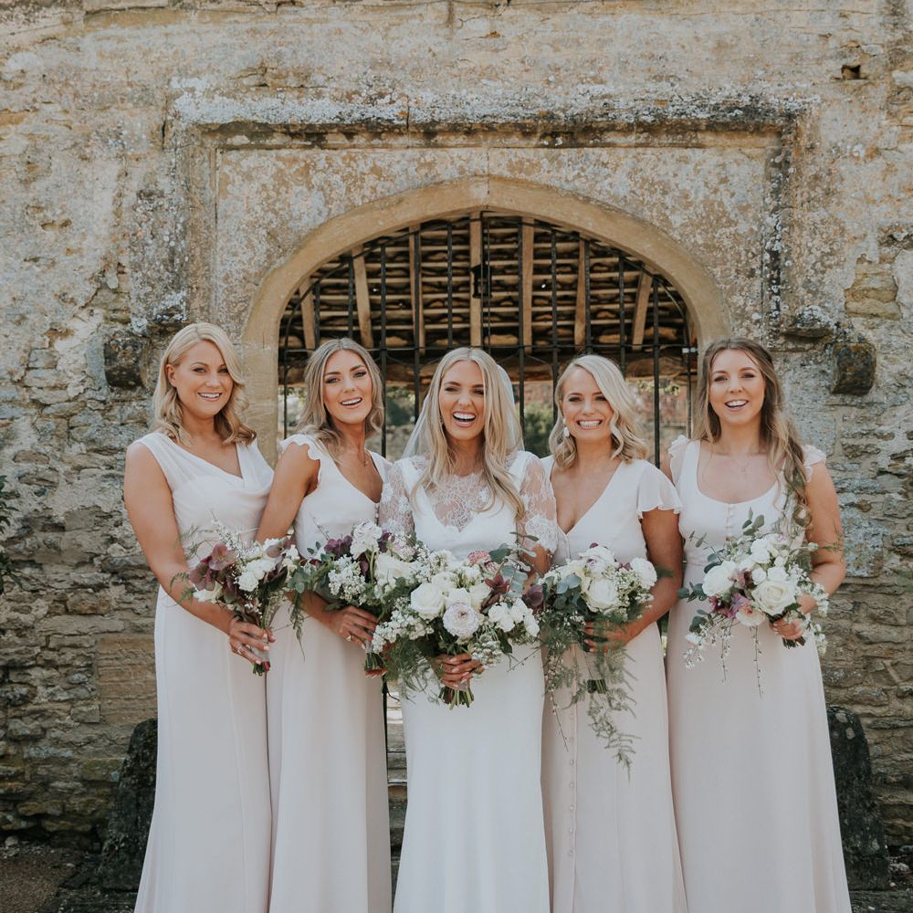 Blonde with with long wavy hair in a Charlie Brear wedding dress with lace caplet with her bridesmaids in white dresses 