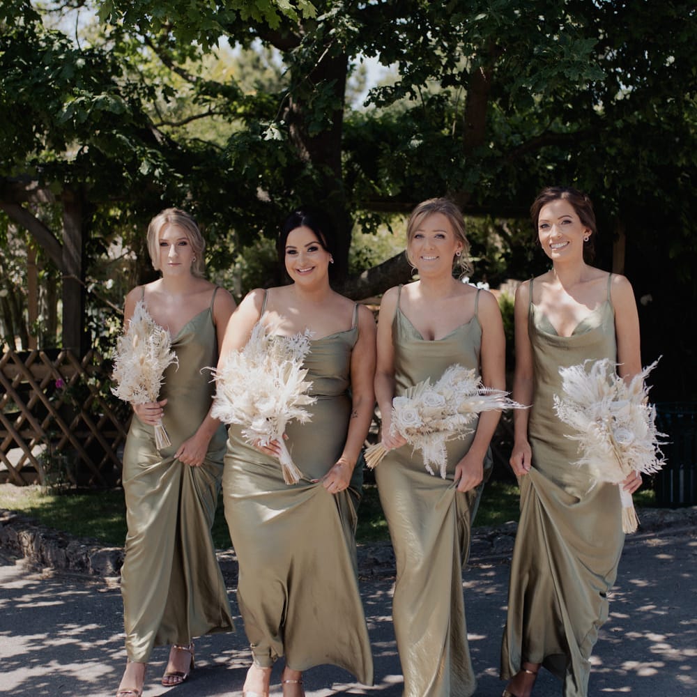 Bridesmaids in green satin midi dresses holding neutral beige dried flower bouquets 
