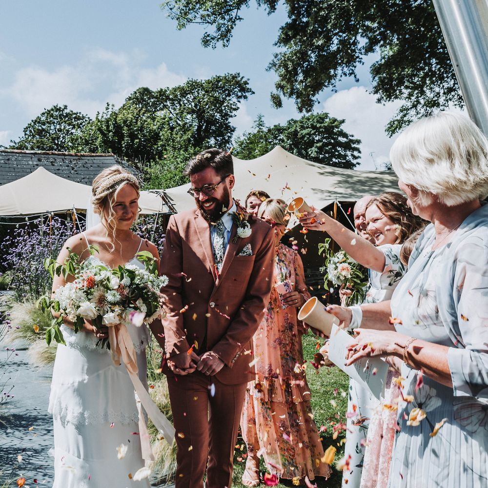 Bride & walk groom together outdoors on sunny day in Cornwall as bride carries floral bouquet