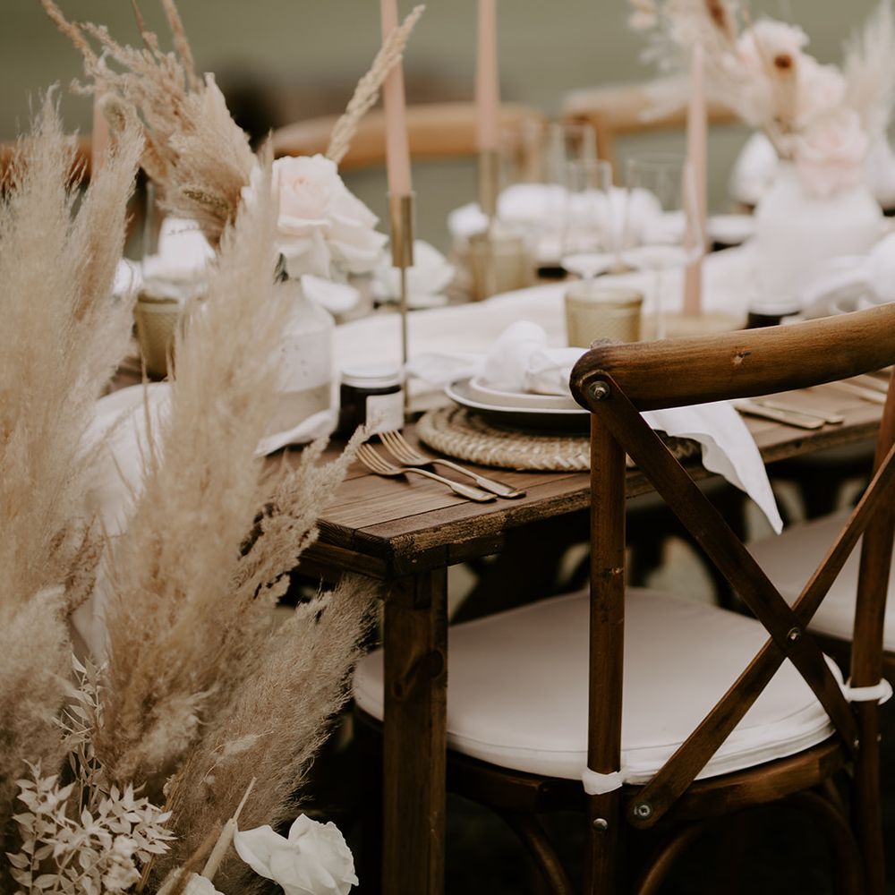 Wooden table with gold candlesticks and cutlery, pink flowers and taper candles 