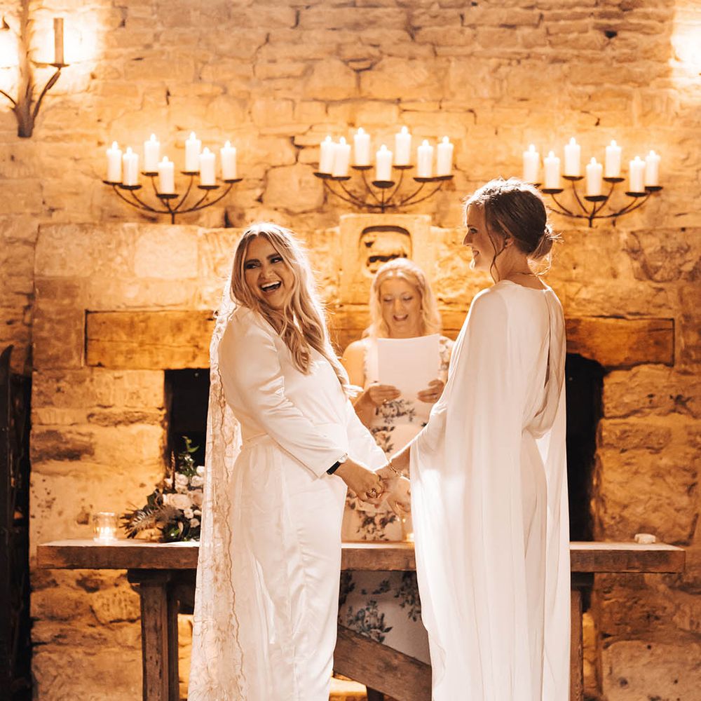 Brides stand in front of limestone wall with candles as they say their vows to one another