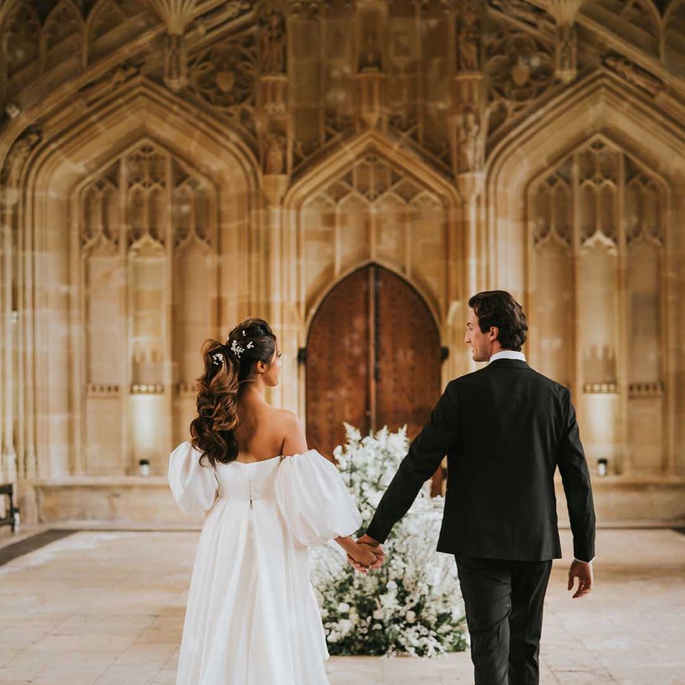 Groom in a black tuxedo holding hands with his bride at their monochrome Bodleian wedding reception