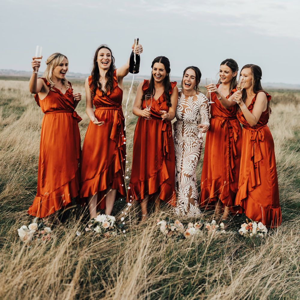 Bridal party were silk orange ruffle low cut dresses as they open the champagne with Boho Bride at Elmley Nature Reserve