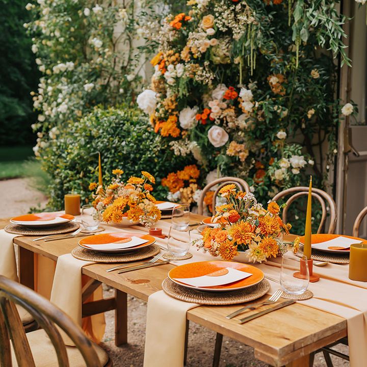 Outdoor wedding table decor with natural furniture, orange flowers and tableware 