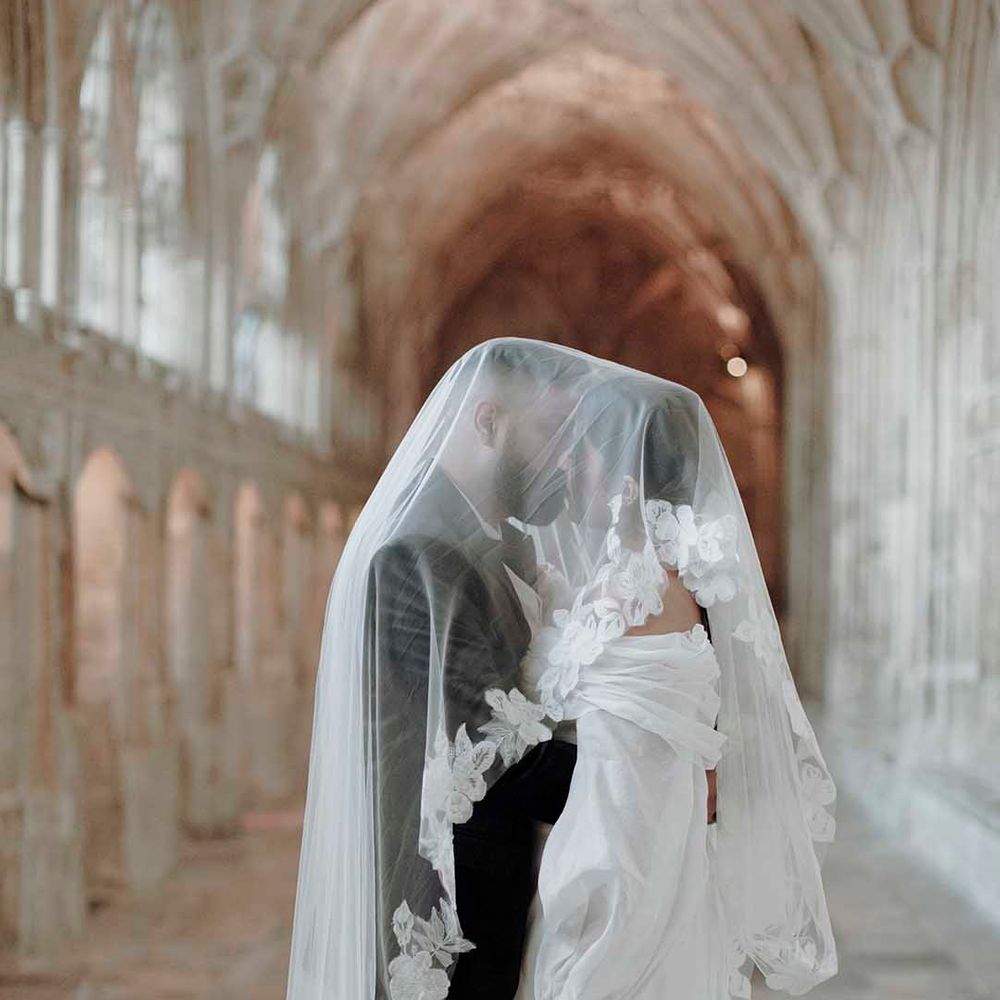 Bride and groom kissing in a medieval wedding venue corridor with a lace edge veil over them 