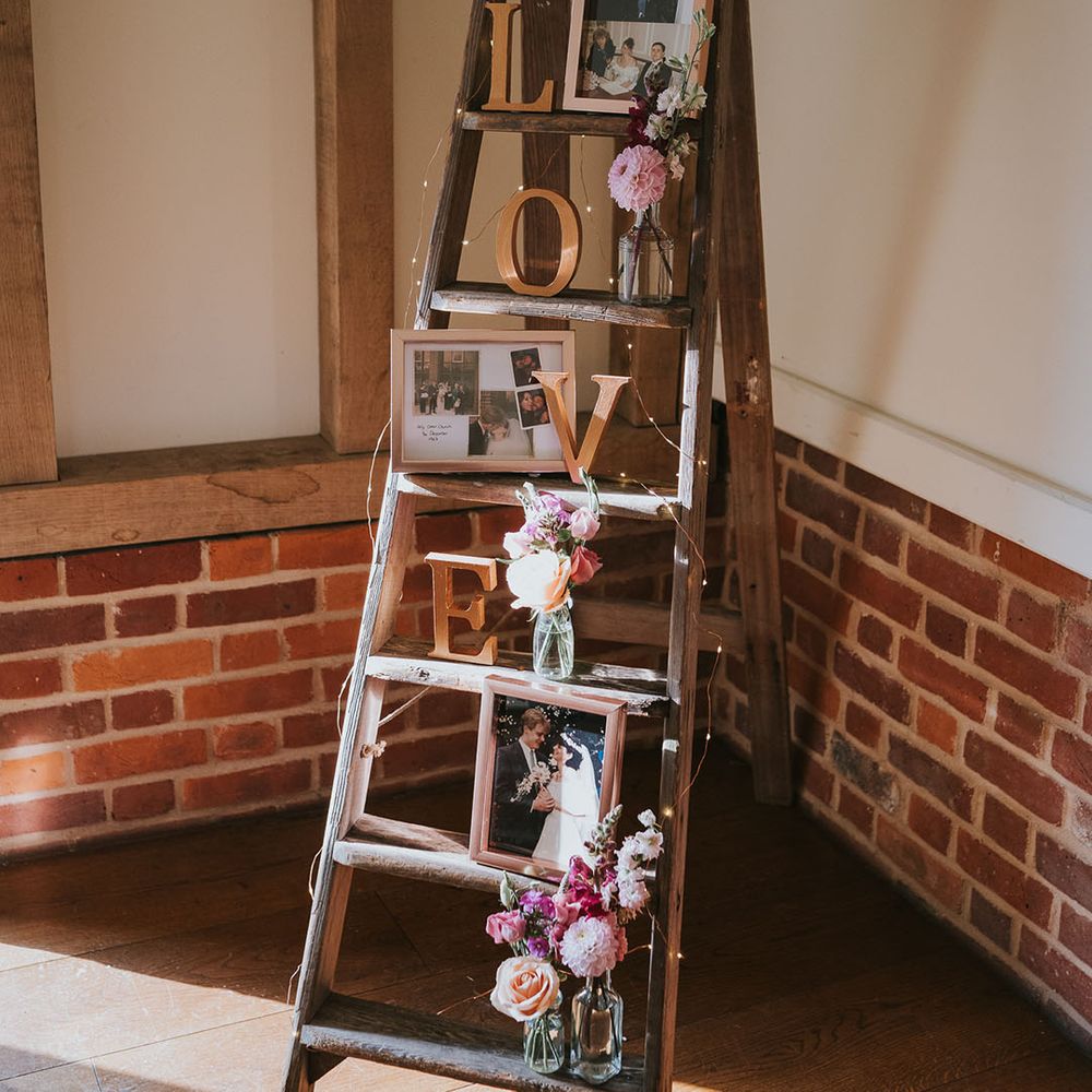 Wooden ladder rustic wedding decor with family photos and small vases of pink, red and white flowers