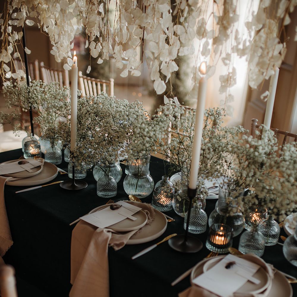 wedding table decor with gypsophila stams in glass bottles, black table cloth and beige tableware and linens 
