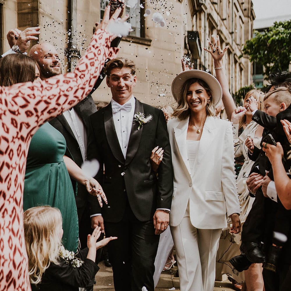 Bride in pearl Nadine Merabi trouser suit and groom in black tie with blue bow tie 
