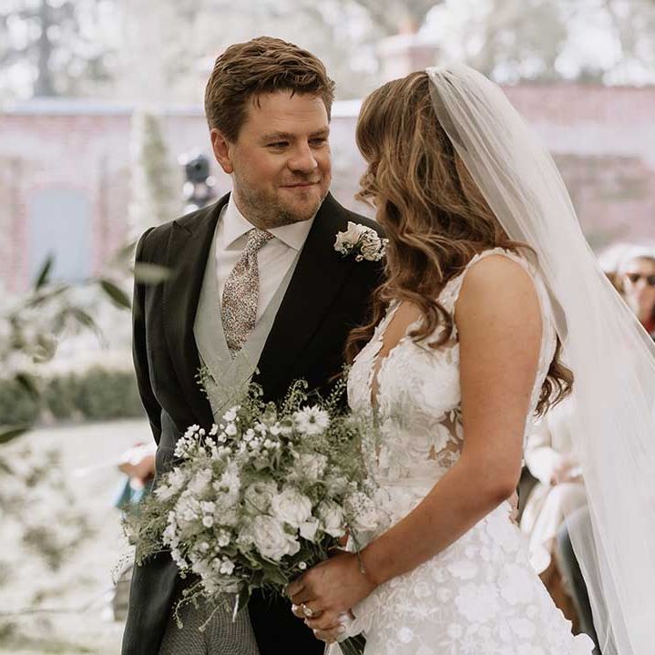 Groom looks intently into the bride's eyes as they stand at the altar together with groom in morning suit with green waistcoat and patterned tie 