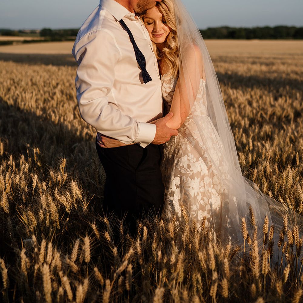 Bride lays her head on the groom's chest as they share a hug during golden hour on their wedding day 