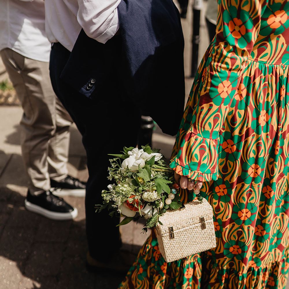 Bride holds woven purse with brightly beaded handle and holds white floral bouquet 