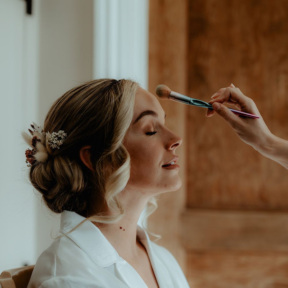 Bride wearing a white robe gets her makeup done for her wedding day 