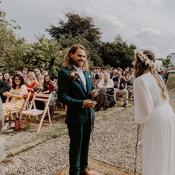Bride & groom during handfasting ceremony outdoors on their wedding day with boho feel 