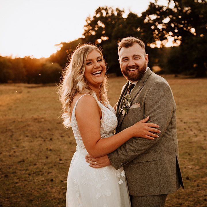 The bride with curled blonde hair laughs with the bearded groom for their cute couple portraits 