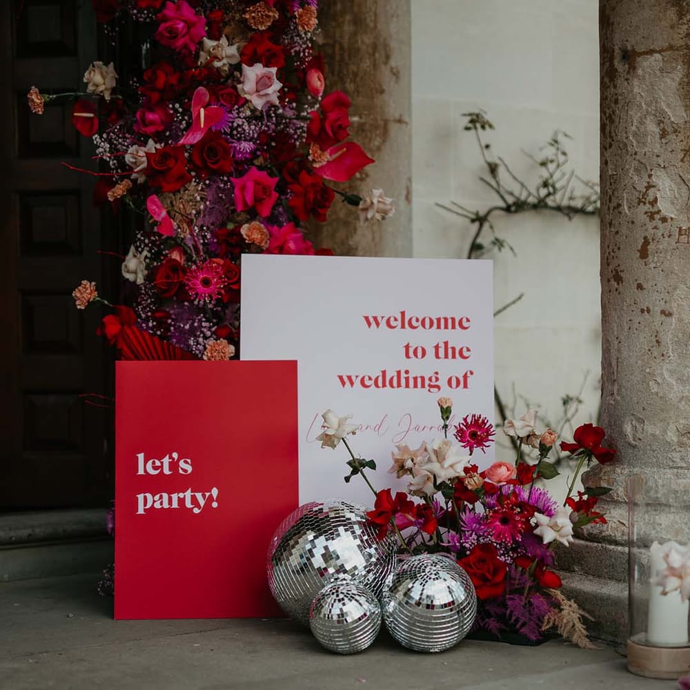 Floral decorations with magenta and pink dahlias, orchids, roses, amaryllis, anthuriums and dried flowers with three disco ball wedding decorations and retro wedding signs