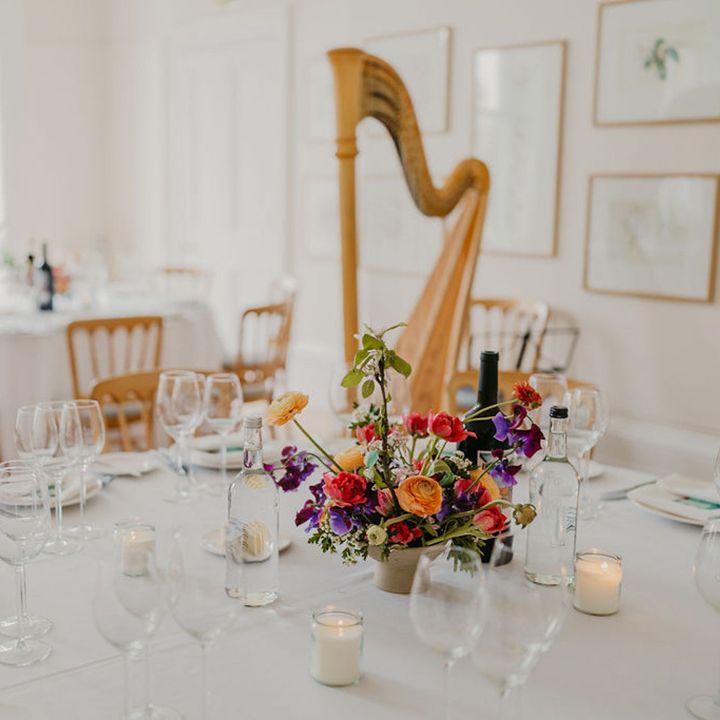 Gold harp beside round tables covered with white tablecloth finished with brightly coloured floral centrepiece 