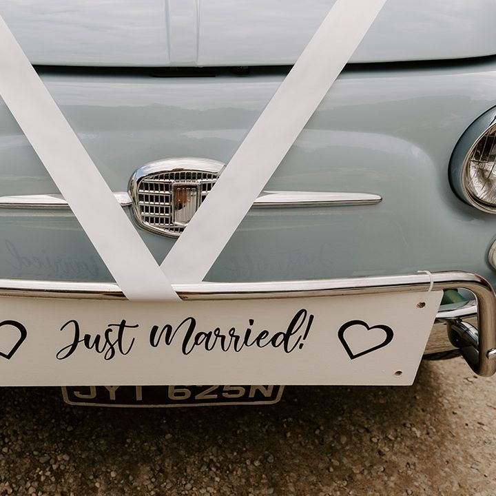 White 'Just Married' sign attached with white ribbon to the light blue vintage Fiat 500 wedding car 